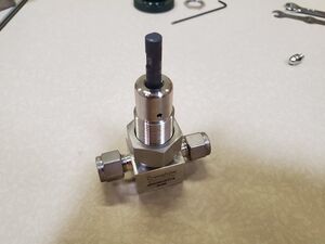 A assembled bellows-sealed valve after it has had the copper tip installed into the stainless steel stem sitting on its base on top of a table.