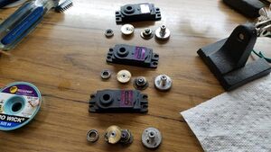 Three servo boxes on a table with their gears, bearings, shafts and screws removed and set beside the servo it came from.