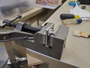 A vise grip with the pin clamped inside on a worktable with the gear still inside.